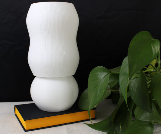 Lamp tuned off, displayed on a book next to a monstera plant